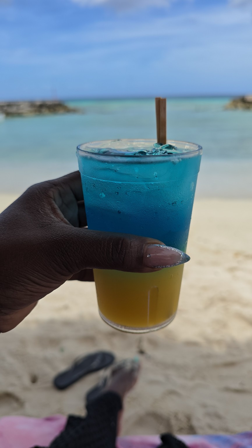 Rhode holding a colorful drink with Aruba’s turquoise water in the background